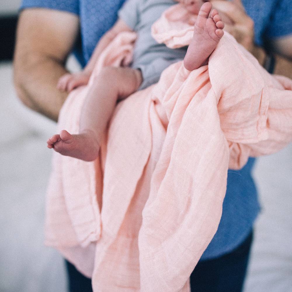 Lightweight cotton muslin swaddle in Rose Petal, perfect for cozying, nursing, and secure sleep for infants.