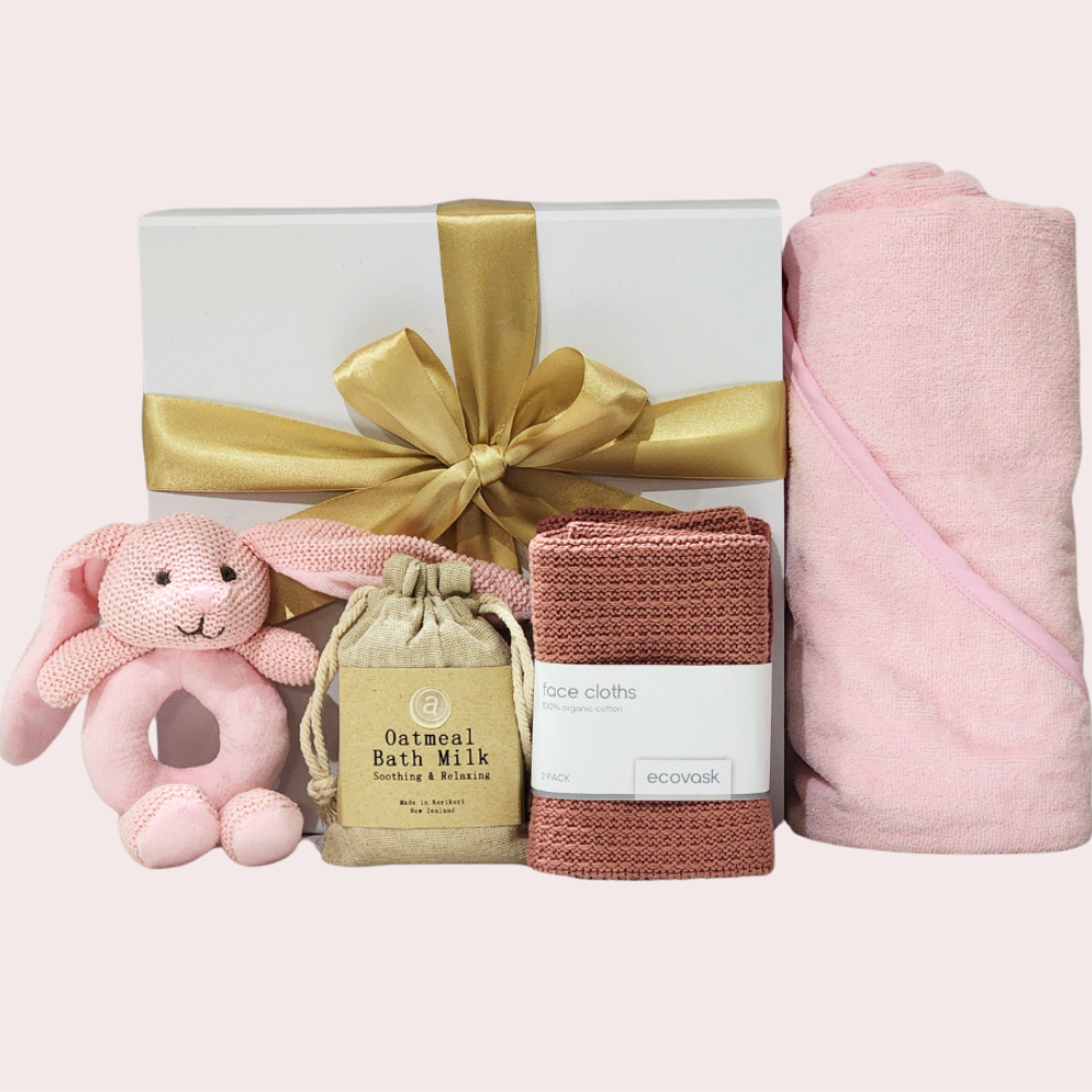 Soft pink baby gift set featuring a hooded towel, bunny rattle, bath milk, and organic facecloths for newborn comfort.