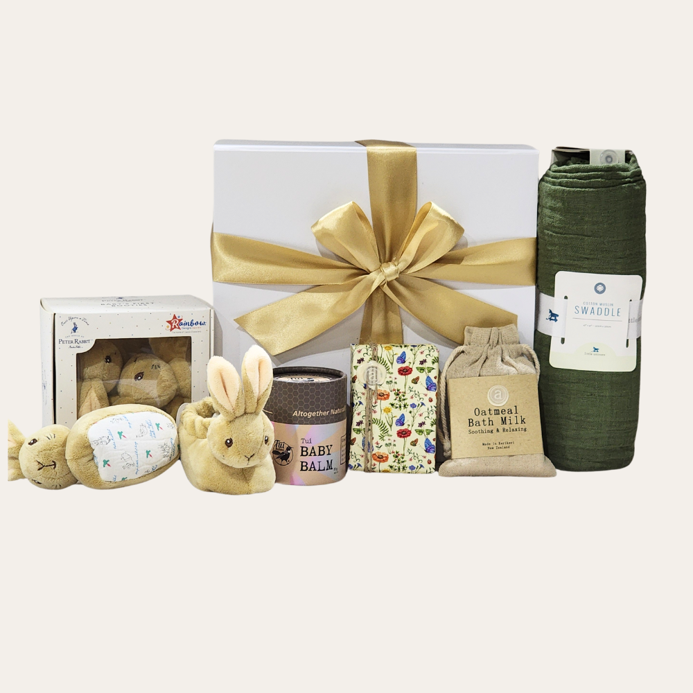 Luxurious baby gift box featuring cozy booties, a swaddle, soothing balm, soap, bath milk, and elegant presentation.